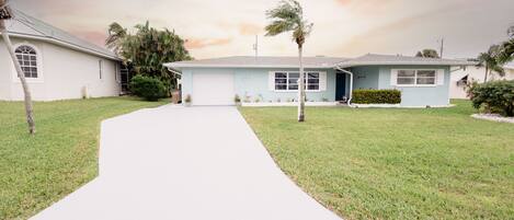 A single-story house with a front yard, a driveway, and a palm tree.