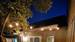 Un espace patio aménagé avec une table et des chaises en bois, un barbecue et des guirlandes lumineuses.