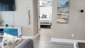 Un salon moderne avec un canapé, un téléviseur à écran plat et un tableau représentant une scène de plage.