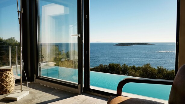 Habitació moderna amb una gran porta de vidre que dona a un balcó amb vista al mar i a una piscina.
