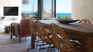 Una zona menjador moderna amb una taula gran, cadires de vimet i vista a l'oceà.