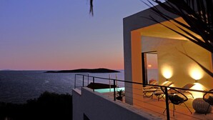 Edifici modern amb un balcó que domina el mar, on es poden veure gandules i una piscina.