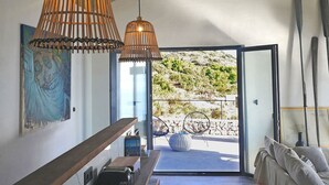 Un interior modern amb una finestra gran, una banca de fusta, un sofà i dues làmpades de vimbla penjades.