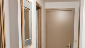Un pasillo con suelo de madera, paredes blancas y una puerta cerrada al final.