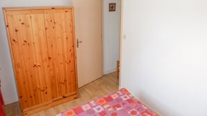 A room with a wooden wardrobe, a door, and a bed with a patterned bedspread. - Homerez - Apartment in Allevard (Allevard)