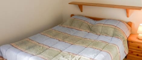 Ein Schlafzimmer mit einem Bett, einem hölzernen Kopfteil, einem Nachttisch und einem an der Wand befestigten Regal.