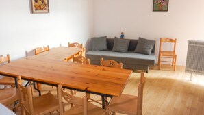Una habitación con una mesa de comedor de madera y sillas, un sofá gris con cojines, y dos cuadros florales enmarcados en las paredes.