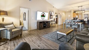 A spacious living room with a large TV, a dining area, and a kitchen. - 2 Bedroom, 2 Bathroom Golf Condo featuring Private, Covered Balcony with Pool View (Branson)