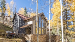 A rustic cabin with stone walls and a sloped roof, surrounded by tall trees and a clear sky. - HAVEN ON HANG GLIDER (Mountain Village)