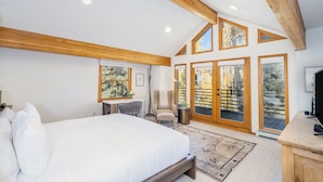 A bedroom with a large bed, wooden ceiling beams, a desk, a chair, and a TV. - HAVEN ON HANG GLIDER (Mountain Village)
