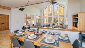 A dining area with a wooden table set for six, surrounded by chairs, with a large window providing a view of autumn trees. - HAVEN ON HANG GLIDER (Mountain Village)