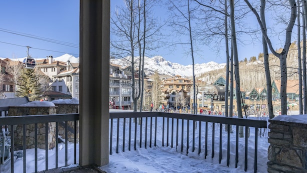 Un balcone coperto di neve con una vasca idromassaggio, con vista su una città, edifici e montagne sullo sfondo.
