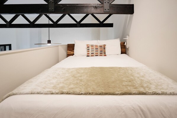 A bed with a white duvet, a fluffy beige throw, and a patterned pillow.