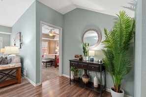 A hotel room with a wooden floor, a desk with a lamp, a dresser with a mirror, and a large potted plant. - Enjoy More Space, More Privacy and Easy Access to Branson's Shows, Shopping and Golf (Branson)