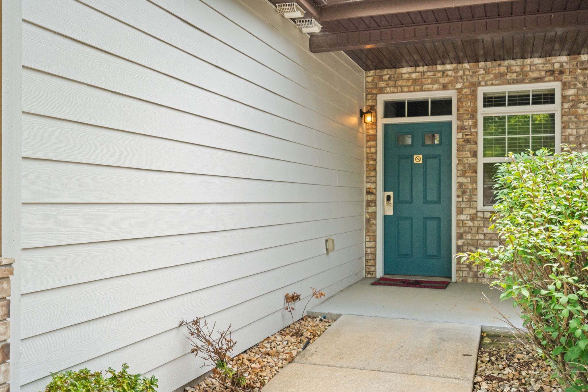 A house with a white siding exterior, a blue door, and a brick foundation.