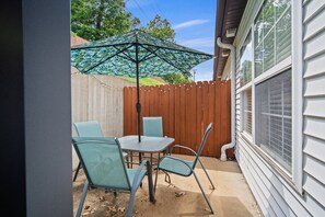 A patio with a table and chairs, a decorative umbrella, and a wooden fence.