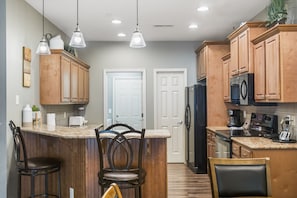 A kitchen with wooden cabinets, a central island with bar stools, a refrigerator, and a microwave.