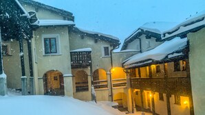 A snow-covered courtyard with a building featuring arched doorways and a balcony.