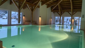 An indoor swimming pool with wooden beams, large windows, and a view of a snowy landscape.