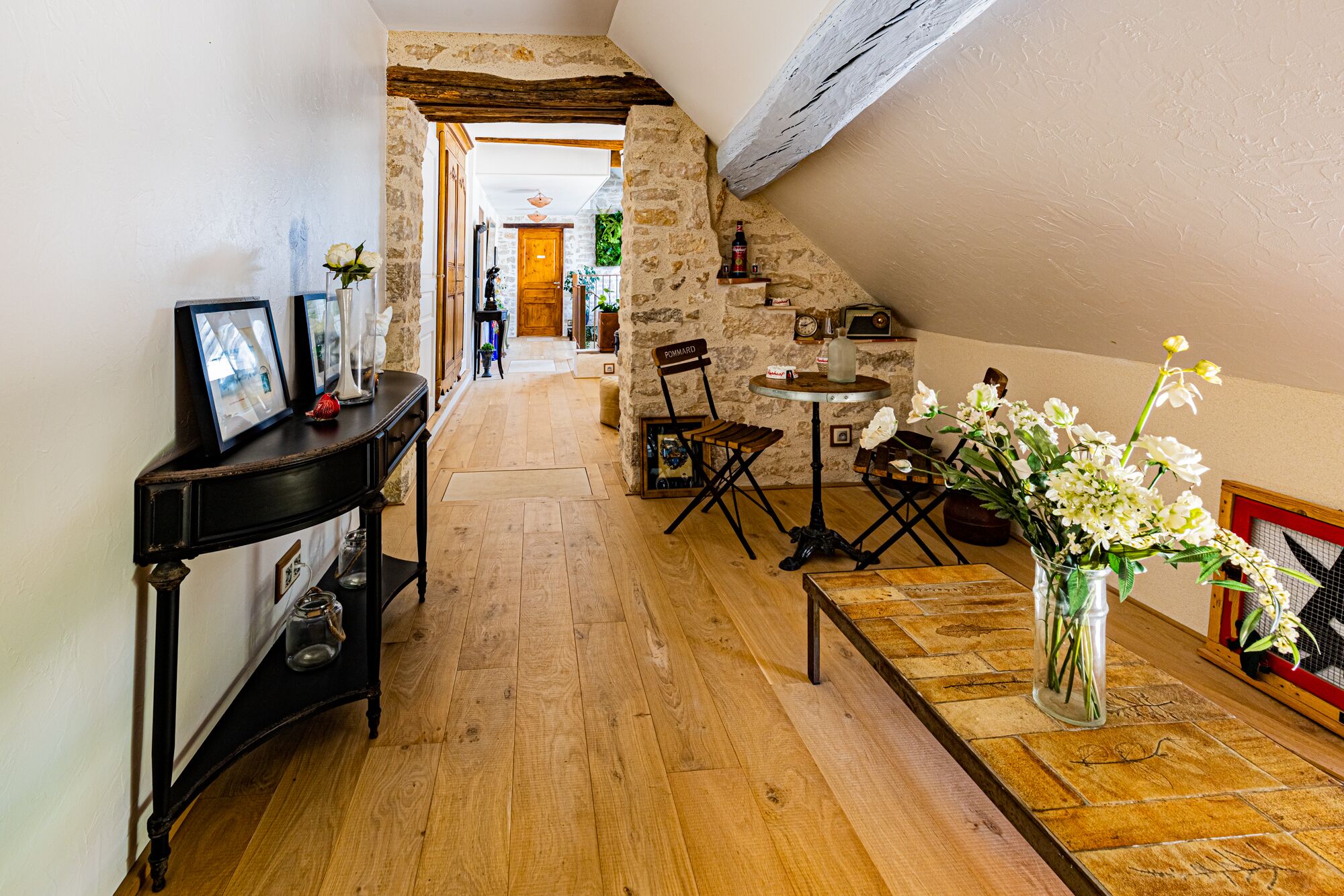 A cozy, rustic interior with a wooden floor, a stone wall, and a small table with a vase of flowers.