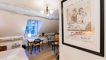 A cozy room with a sloped ceiling, a wooden table with chairs, a window with a view, and a framed poster on the wall.