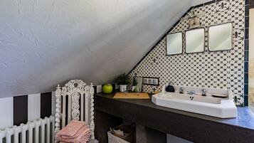 A bathroom with a white radiator, a vanity with a sink, and a mirror above it. There is a decorative headboard and a green apple on the counter.