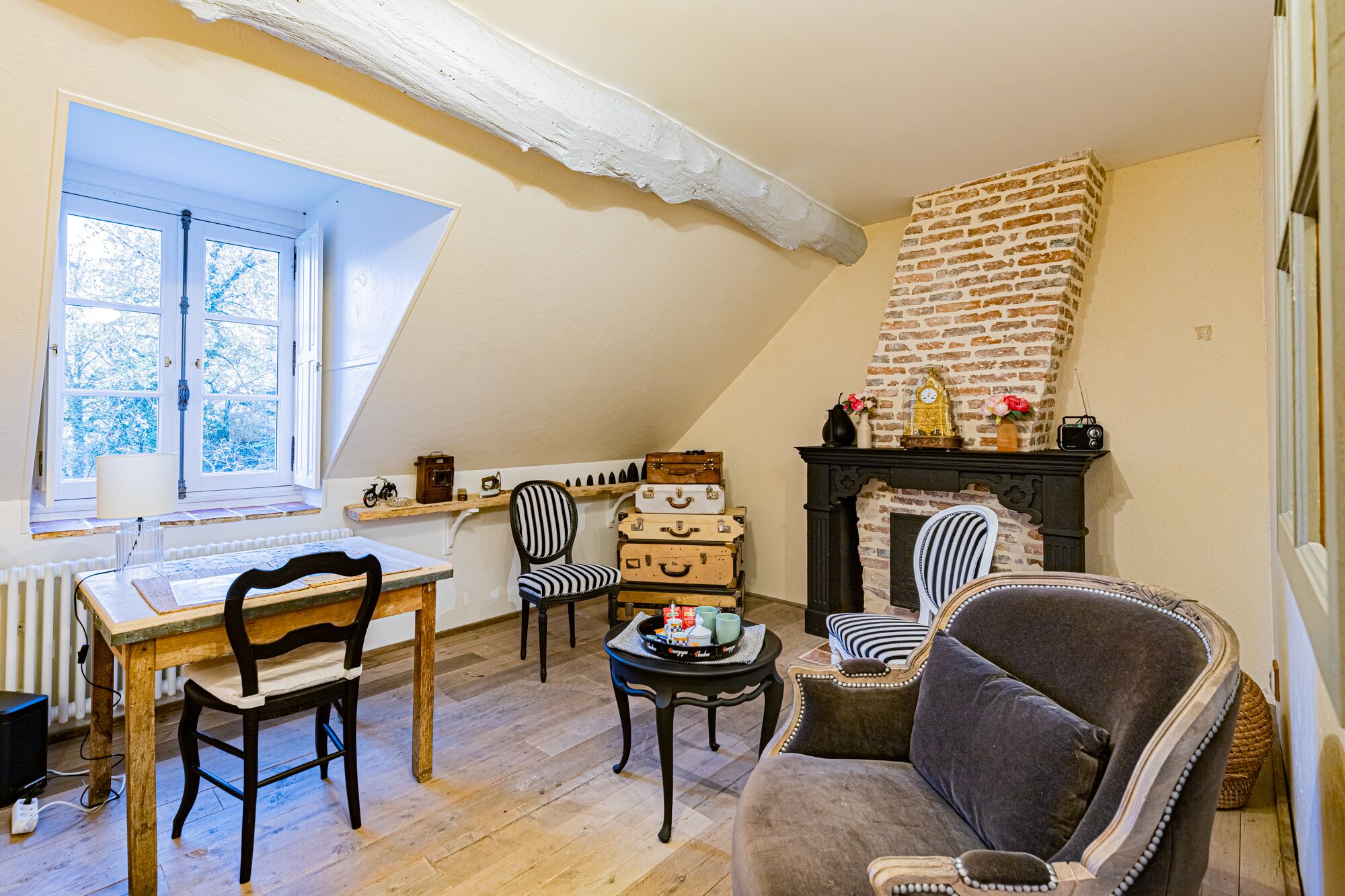 A cozy room with a fireplace, a dining table with chairs, and a window with a view of trees.