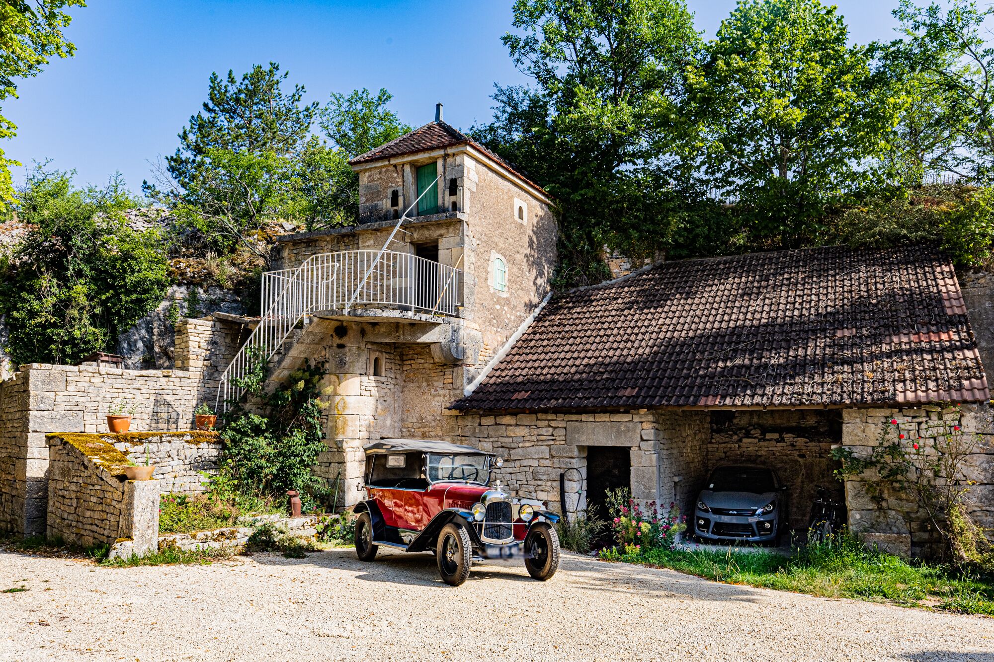 Ein Gebäude aus Stein mit einem Ziegeldach, einer Treppe, die zu einem Balkon führt, und einem Oldtimer davor.