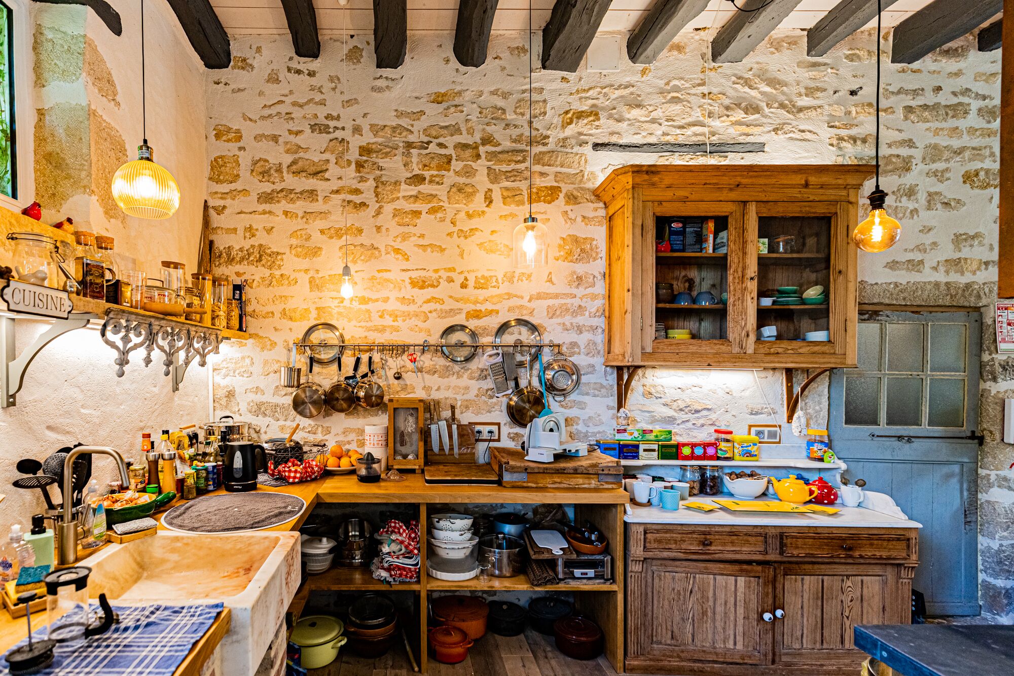 A rustic kitchen with stone walls, wooden cabinets, and various cooking utensils.