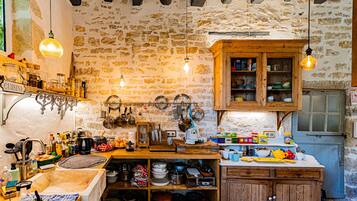 A rustic kitchen with stone walls, wooden cabinets, and various cooking utensils.