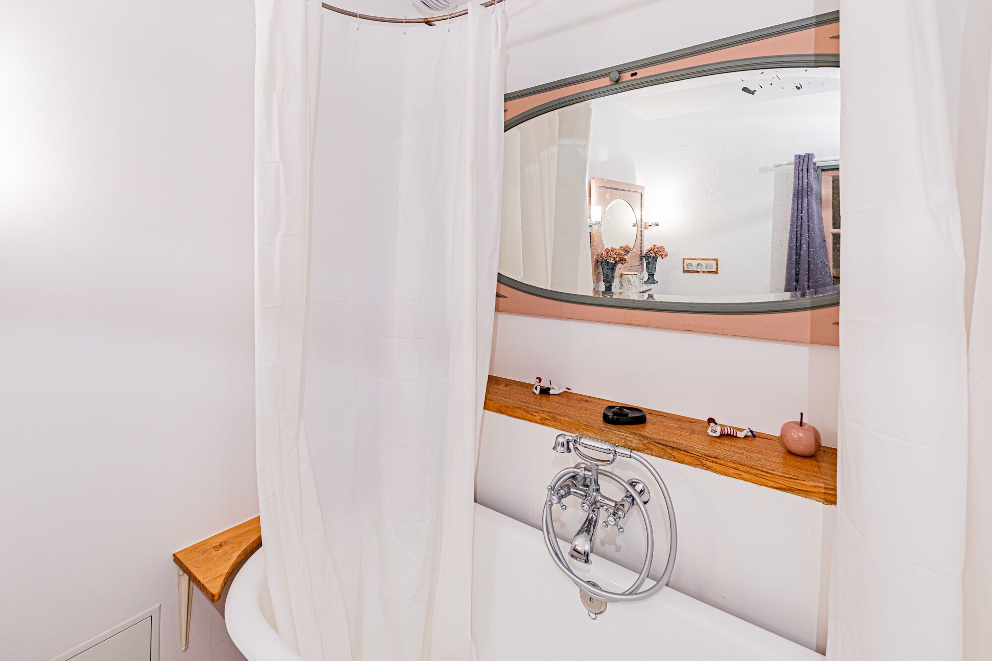 A bathroom with a bathtub, a wooden shelf, a mirror, and a shower curtain.