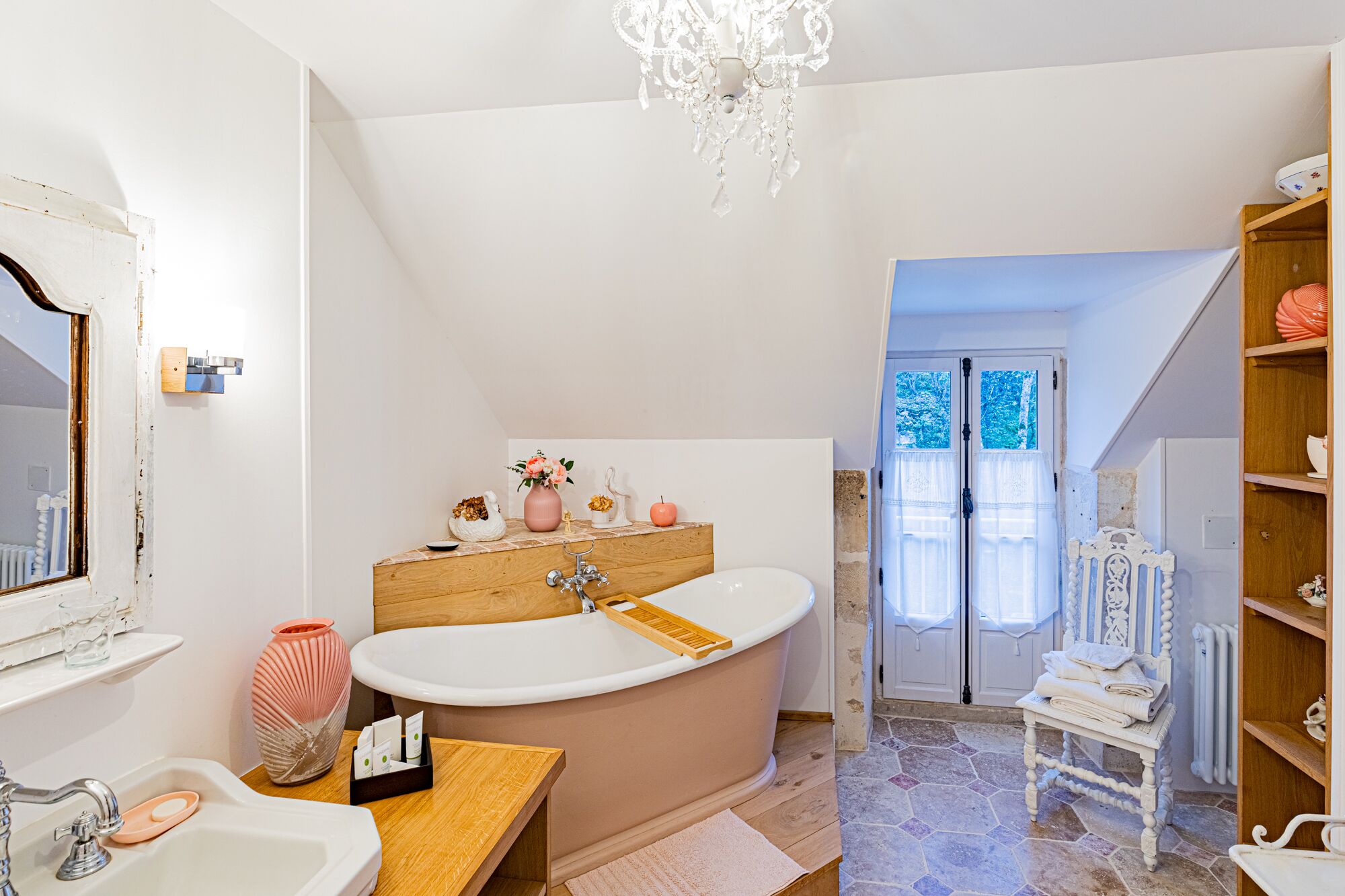 Un baño con una bañera independiente, un tocador con espejo y una araña.