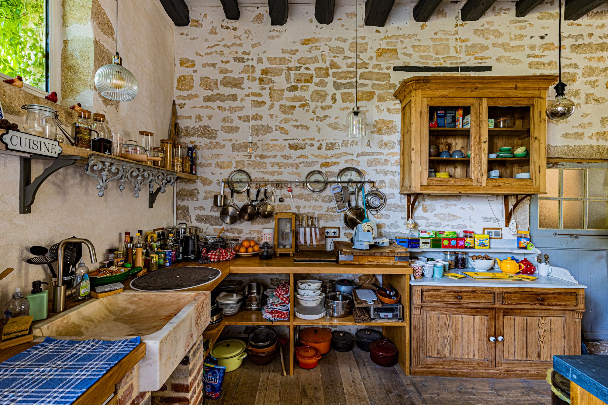 A rustic kitchen with stone walls, wooden cabinets, and various kitchen utensils and appliances.