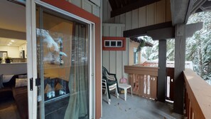 Ein überdachter Außenbereich mit einer Schiebetür, die in ein Wohnzimmer führt, eine Holzterrasse und Blick auf schneebedeckte Bäume.