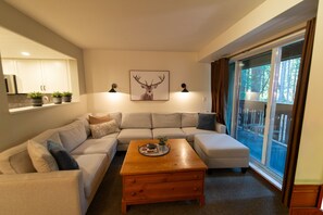 A modern living room with a sectional sofa, a wooden coffee table, and a large window with a view of trees.