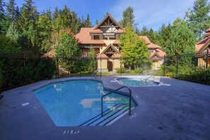 A pool area with two pools, surrounded by a fence and trees.