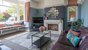 Una sala de estar con chimenea, televisor y un área de descanso con cojines.