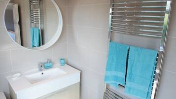 Un baño moderno con un lavamanos blanco, espejo y toallero cromado.