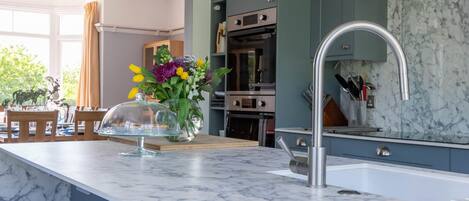 A modern kitchen with a marble countertop, a stainless steel sink, and wooden stools.