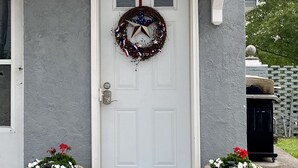 A white door with a star and wreath decoration, flanked by two large planters with flowers. - Carriage House on Main in NRG National Park  (Oak Hill)