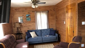 A cozy room with a blue sofa, two patterned armchairs, a wooden ceiling fan, and a small rug on the wooden floor. - Carriage House on Main in NRG National Park  (Oak Hill)