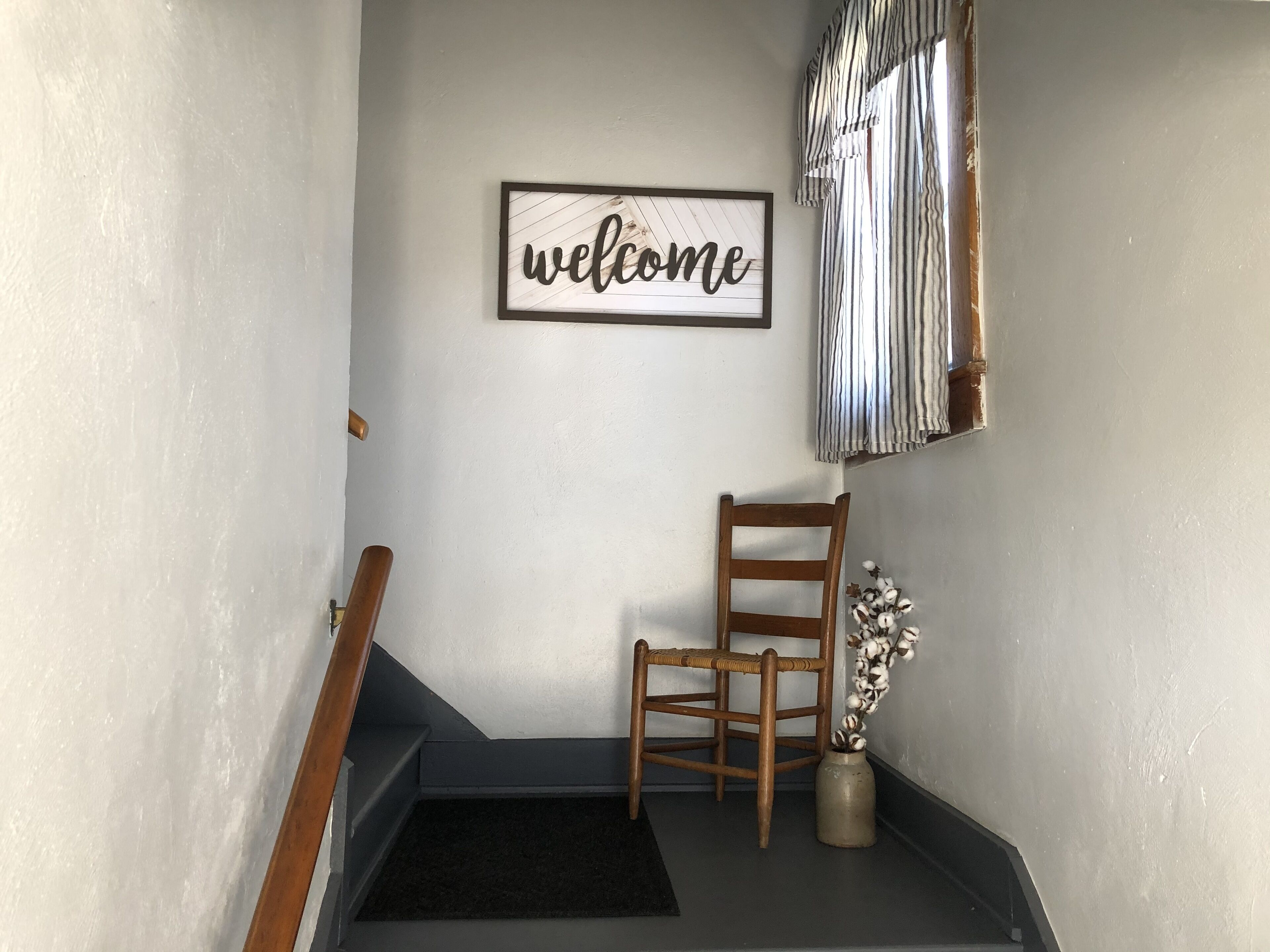 Un escalier avec une chaise en bois et un panneau d’accueil sur le mur.