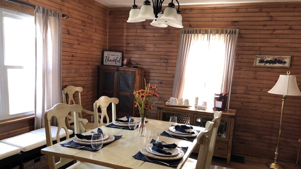 A wooden-paneled dining room with a table set for four, chairs, a vase with flowers, and a sign on the wall. - Carriage House on Main in NRG National Park  (Oak Hill)