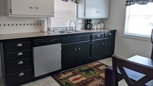 A kitchen with white cabinets, a dishwasher, a coffee maker, and a checkered window valance. - Papa Bear Cottage (Downtown Cody) (Cody)