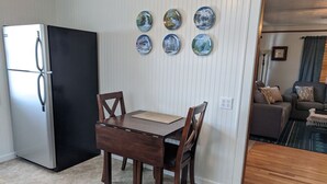 A compact kitchen with a refrigerator, a dining table with chairs, and a wall with six decorative plates. - Papa Bear Cottage (Downtown Cody) (Cody)