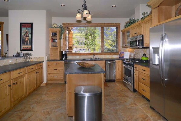 Une cuisine moderne avec des meubles en bois, des appareils électroménagers en acier inoxydable et une grande fenêtre donnant sur la forêt.