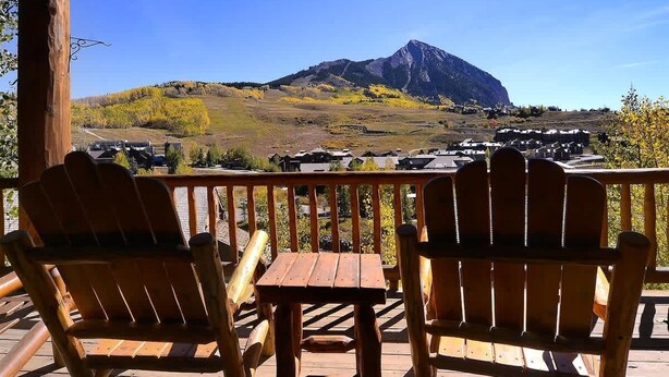 A wooden deck with Adirondack chairs and a table, overlooking a mountainous landscape. - Wildflower Villa (Crested Butte)