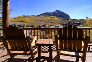 Una terraza de madera con sillas Adirondack y una mesa, con vistas a un paisaje montañoso.