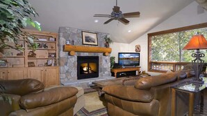 A living room with leather sofas, a stone fireplace, a television, and a ceiling fan. - Wildflower Villa (Crested Butte)