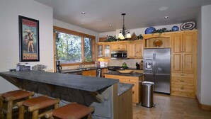 A kitchen with wooden cabinets, a stainless steel refrigerator, a stone island with bar stools, and a large window. - Wildflower Villa (Crested Butte)